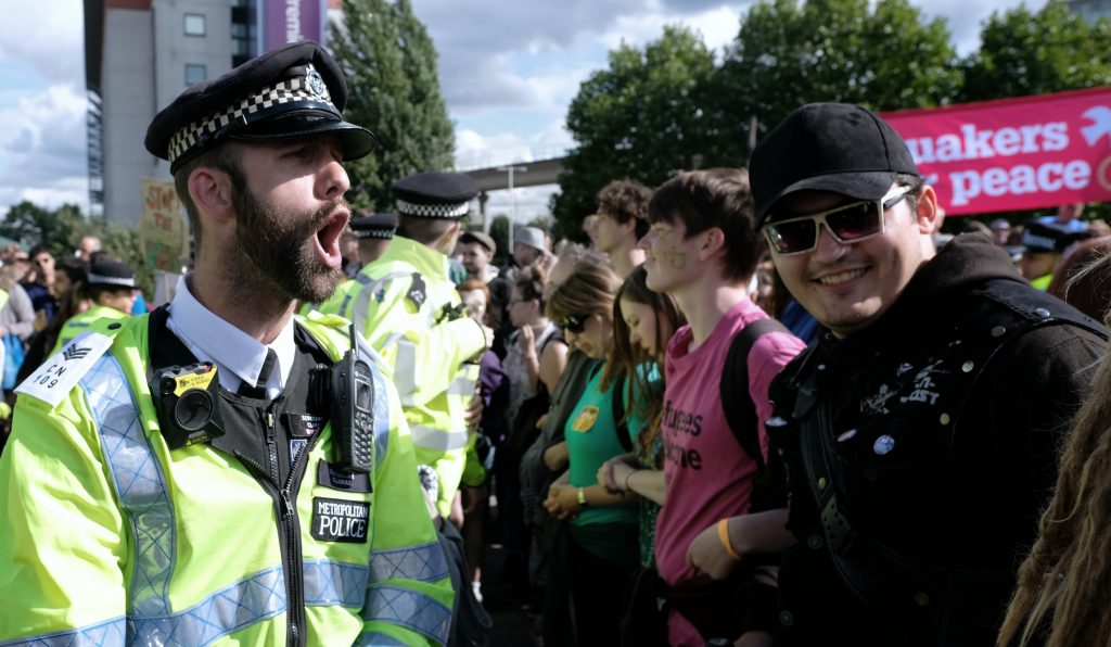 UK police officer shouts instructions at activists protesting against the DSEI arms fair, London, 9 September 2017. (Photo: Alisdare Hickson / Flickr)